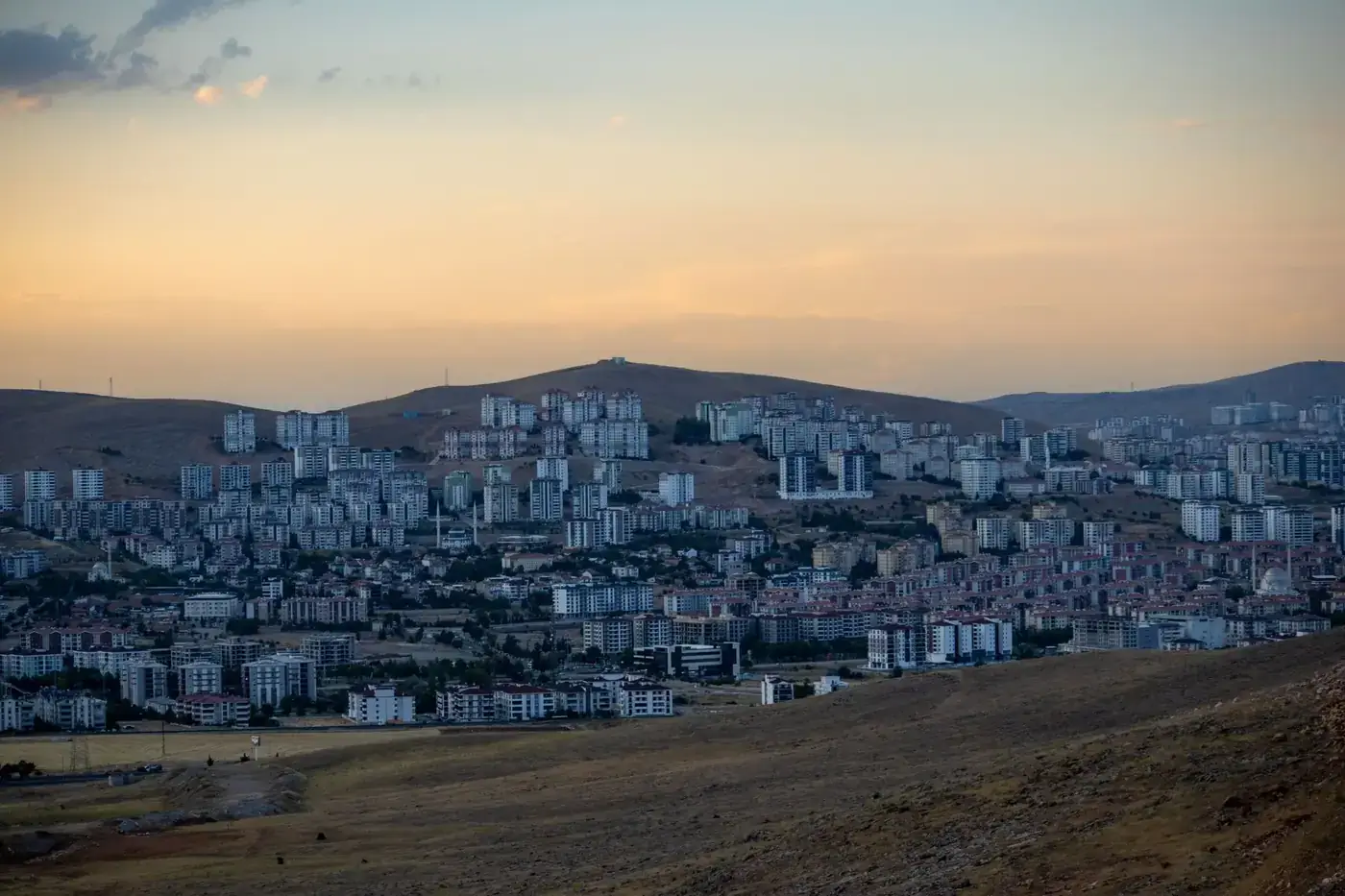 Urban skyline against a scenic hill backdrop during dusk, showcasing architecture and landscape.