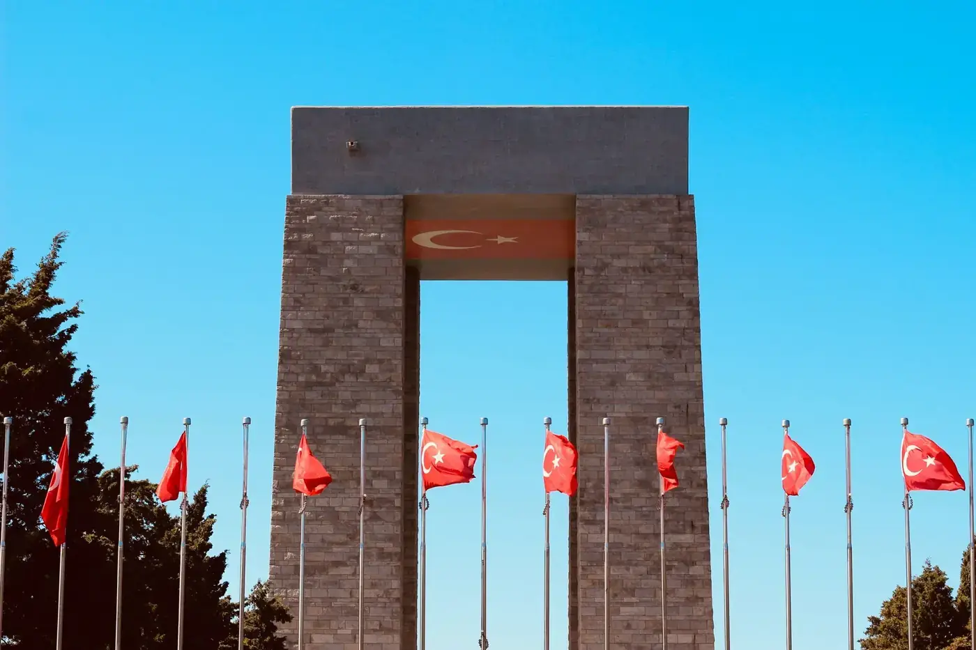 The Turkish national monument with multiple flags waving under a clear blue sky, symbolizing patriotism.