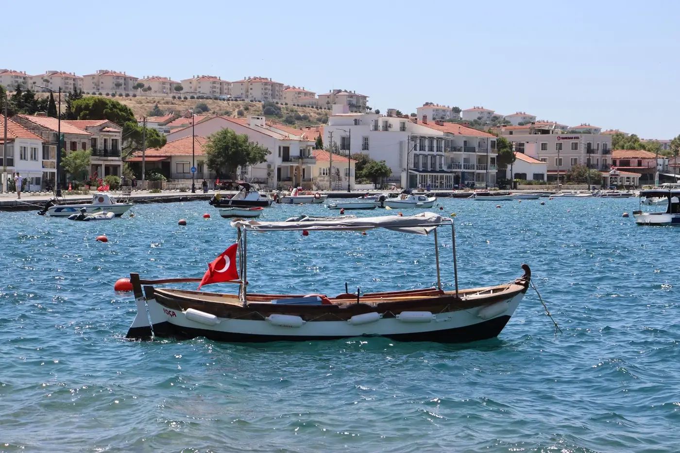 Scenic view of a Turkish harbor with traditional boats and a charming waterfront village under clear skies.