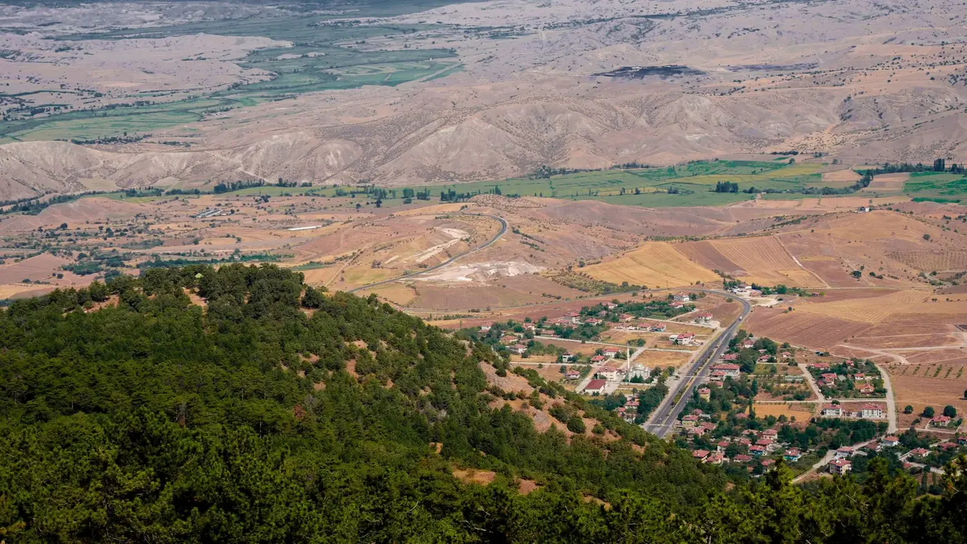 Breathtaking aerial view of Çorum, Türkiye, showcasing hills, farmlands, and a small town under a clear sky.