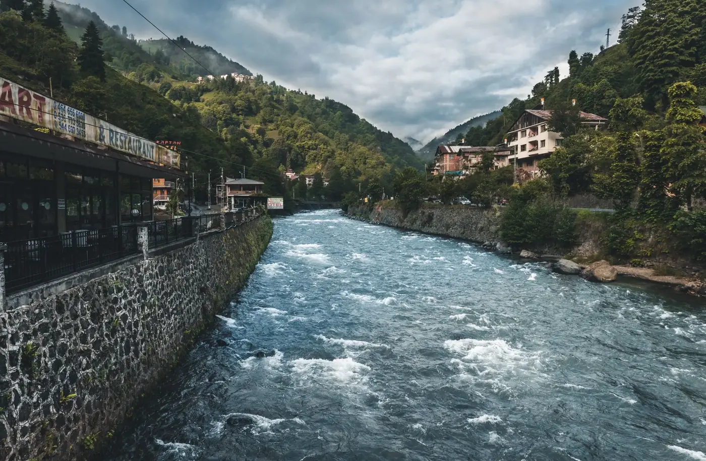 Picturesque view of a river flowing through a village in Rize, Turkey, surrounded by lush green hills.