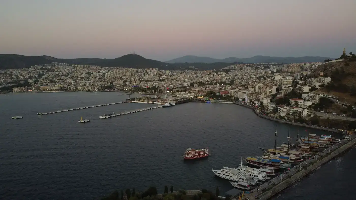Aerial view of Kuşadası harbor at twilight, showcasing a bustling urban landscape by the sea.