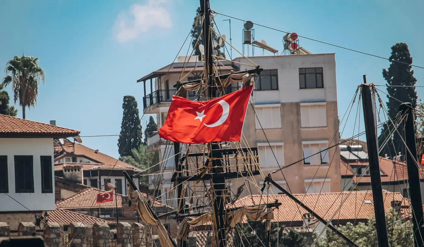 Turkish flag waves prominently on a ship in urban setting with buildings and clear sky.