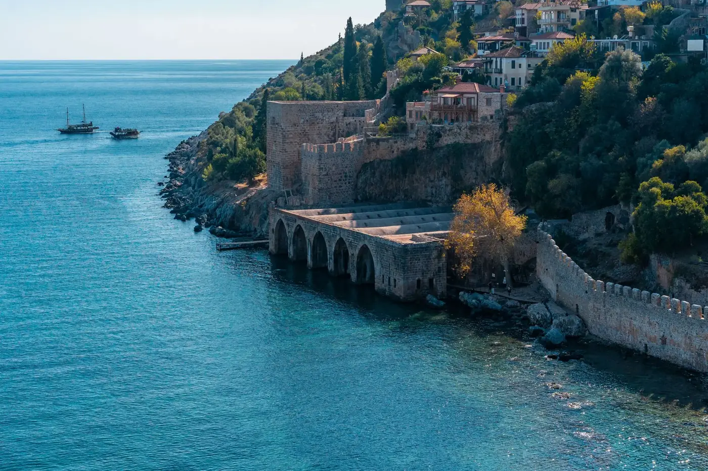 Weathered stone fortress located on rocky seashore with green trees and small settlement with residential buildings near