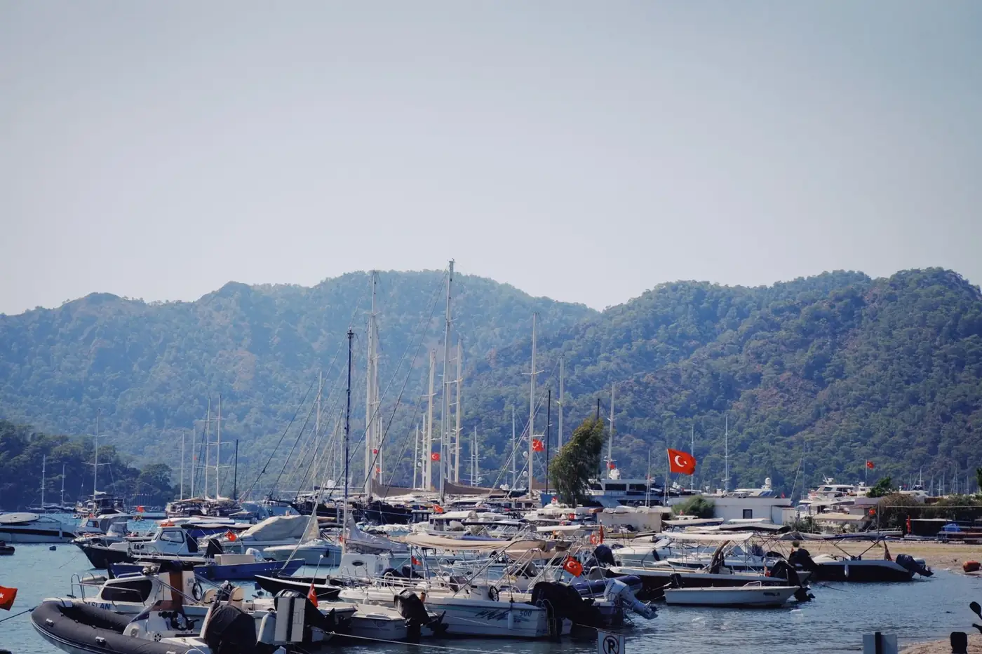 A vibrant marina scene with numerous boats docked against a mountainous backdrop in Turkey.