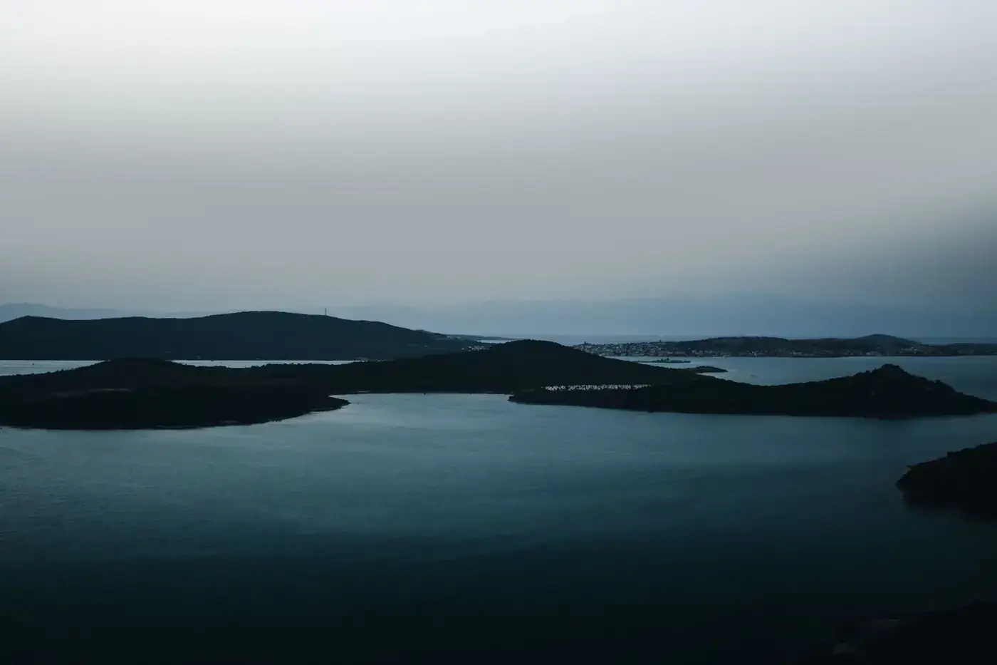 A stunning aerial view of Ayvalık's islands in Türkiye, showcasing calm waters and dramatic hills under a dusky sky.