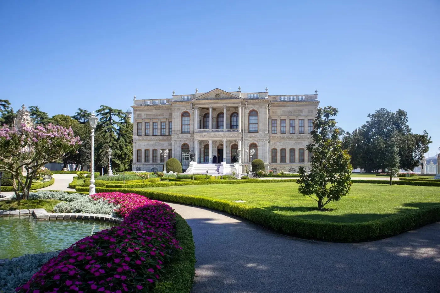 Dolmabahçe Palace with manicured gardens under a bright blue sky in Istanbul, Turkey.