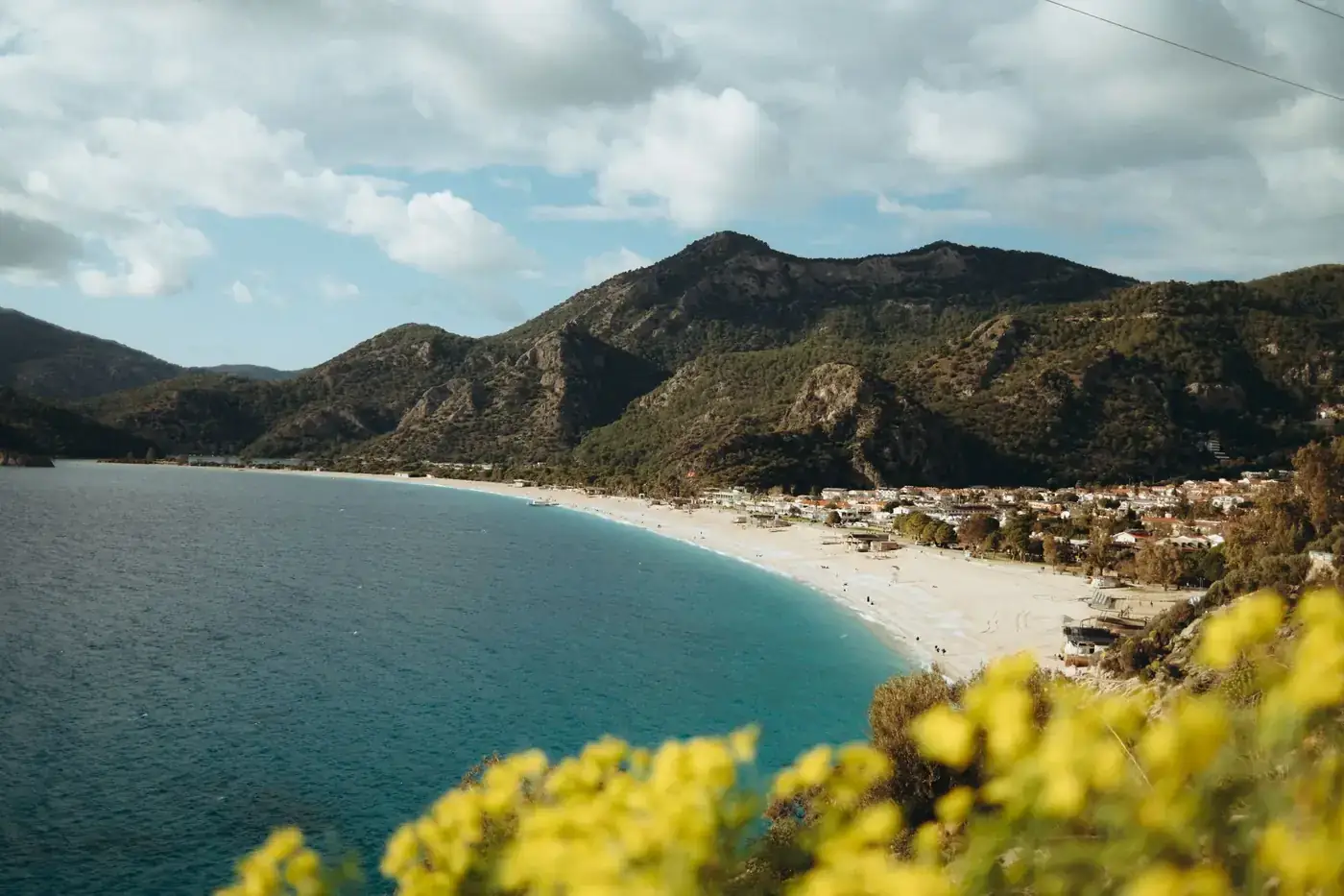 Aerial view of a picturesque Mediterranean beach with mountains and a coastal town in the distance.