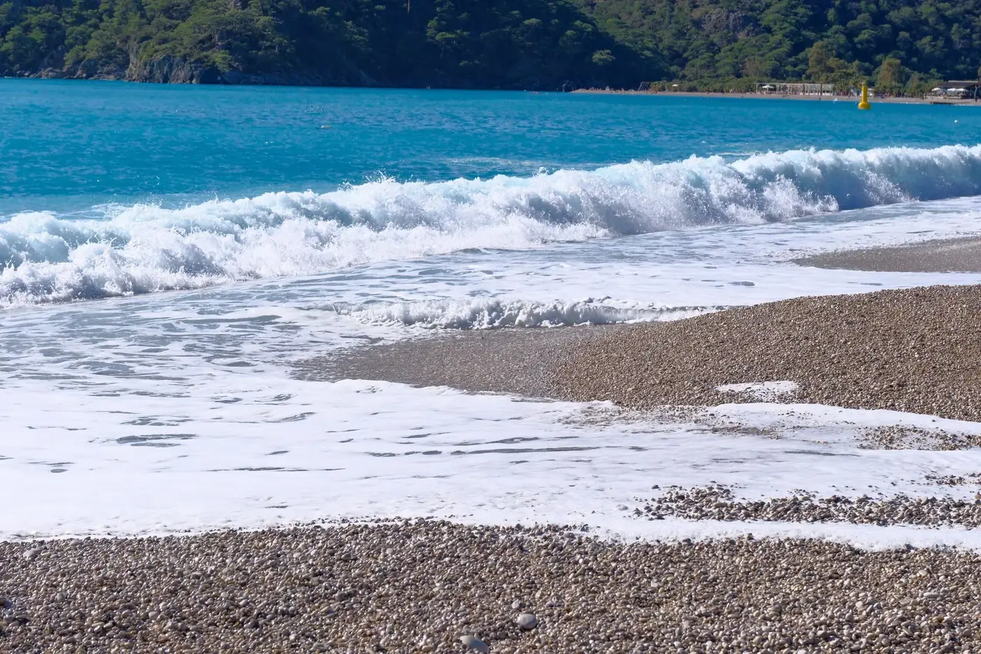 Peaceful view of waves crashing on a pebble beach at Ölüdeniz in Türkiye, capturing the beauty of nature.