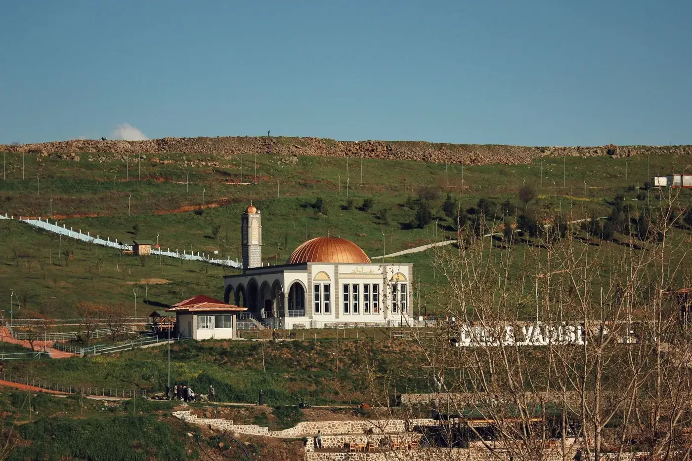 A picturesque mosque with a golden dome surrounded by green hills in Diyarbakır, Türkiye.