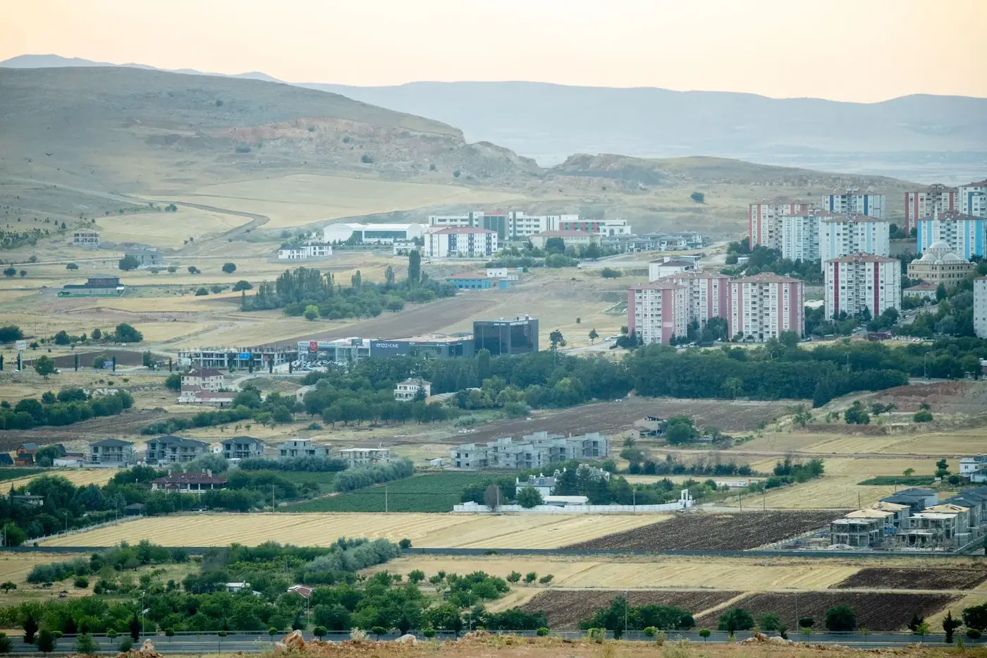 Suburban town with high-rise buildings and fields under a clear summer sky.
