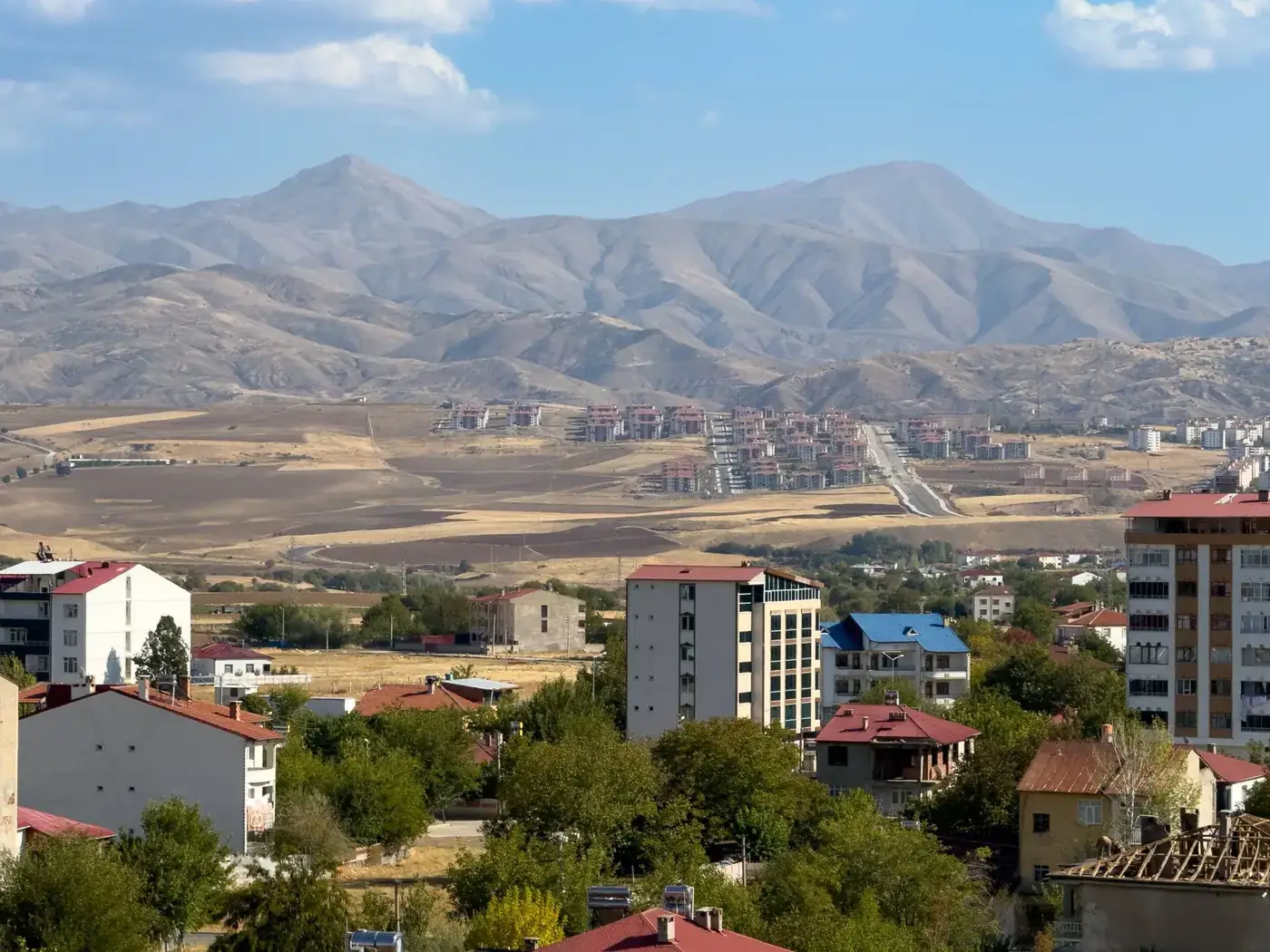 A picturesque landscape of Kovancılar, Türkiye, with mountains and residential buildings under a bright sky.
