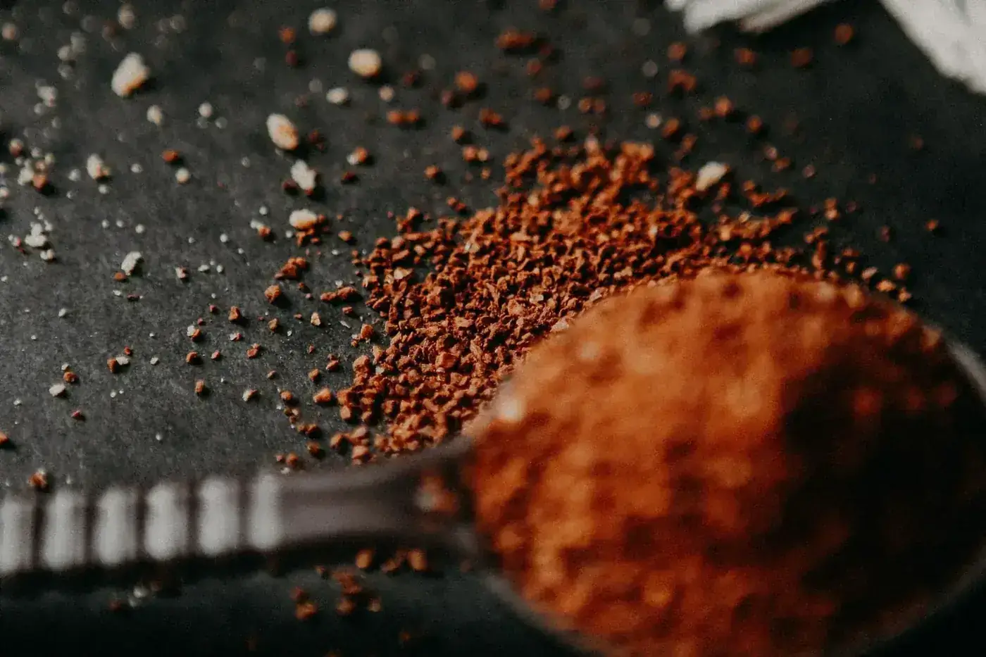 Macro shot of coffee grounds and brown spoon on black surface, showcasing texture.