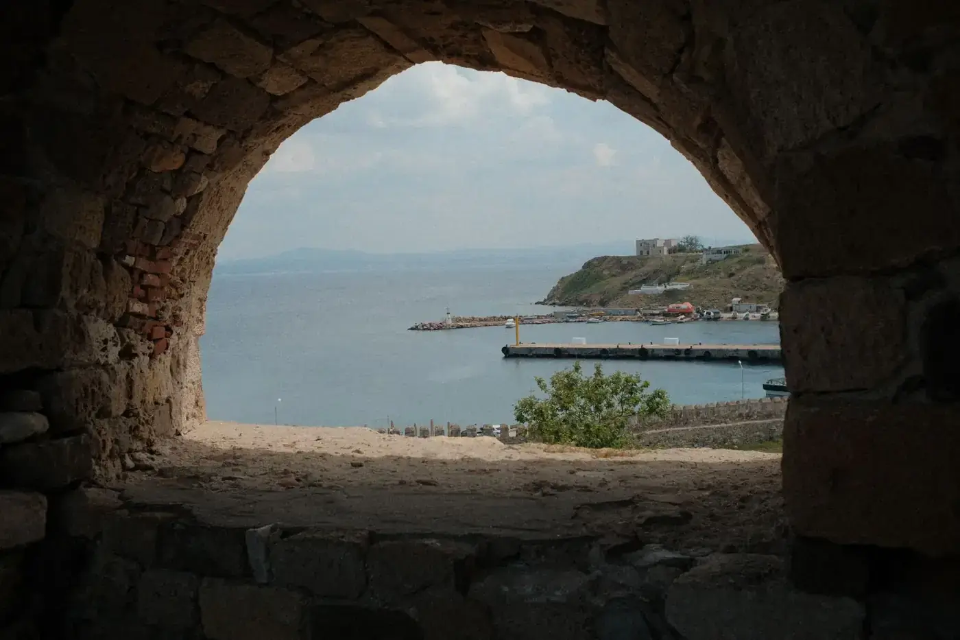A scenic view of Bozcaada harbor through a stone archway, showcasing the island's historic charm.