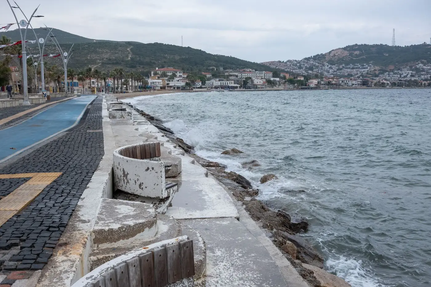 Experience the serene coastline of Foça, İzmir with its charming seashore promenade and distant hills.